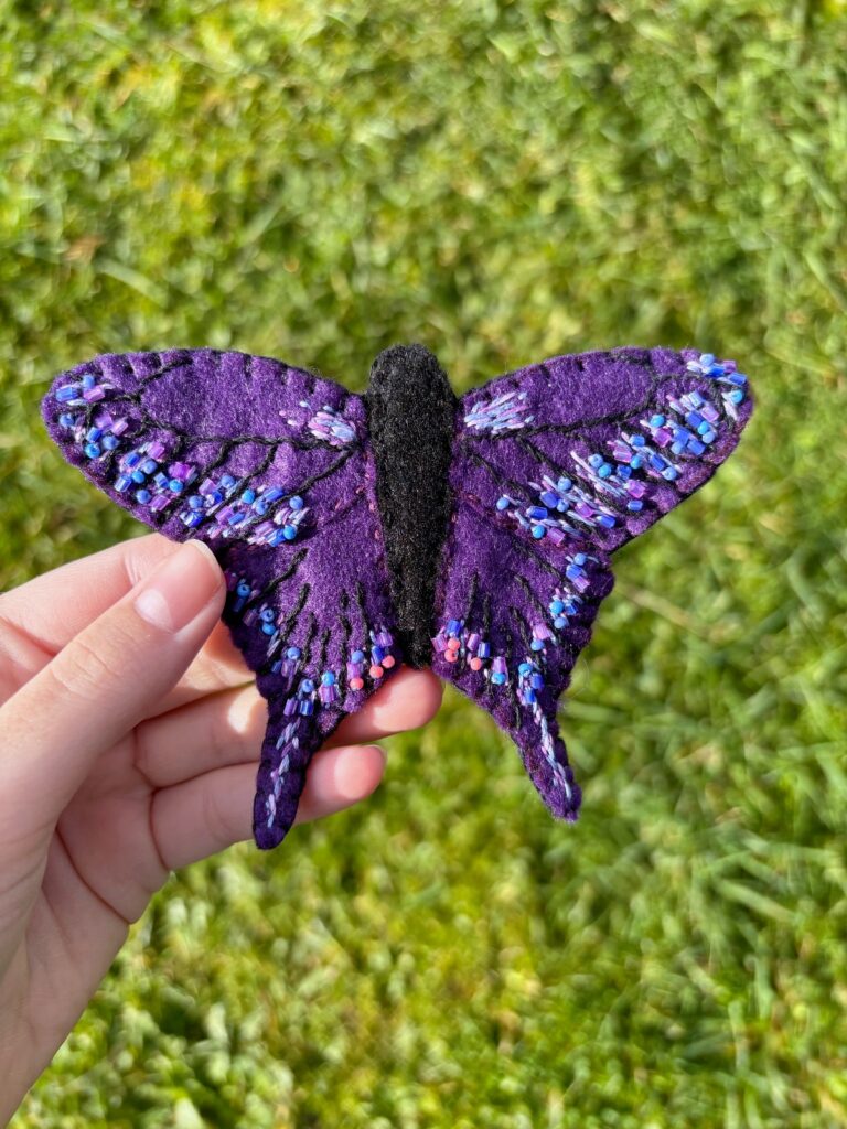 Hand holding finished purple butterfly ornament outside.