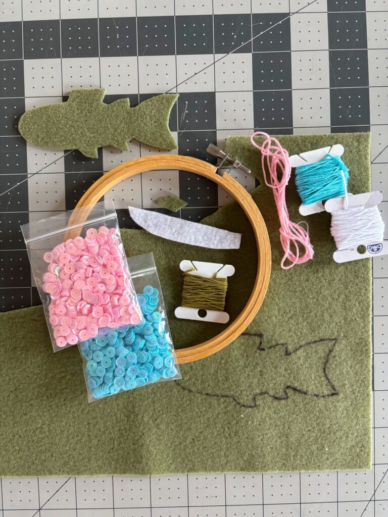 Rainbow trout pattern pieces cut out with embroidery hoop, sequins, and thread on the table.