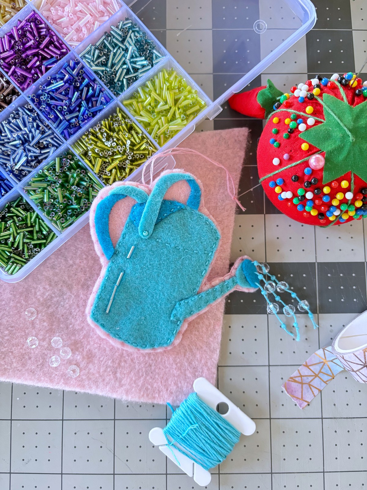 Watering can ornament surrounded by sewing supplies and beads.