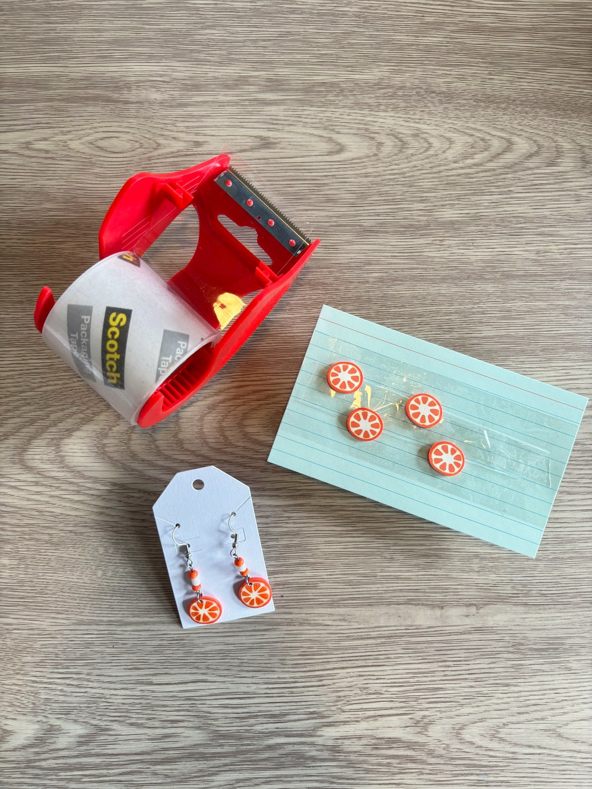 Packing tape and an index card wrapped in packing tape holding polymer clay earrings in place.