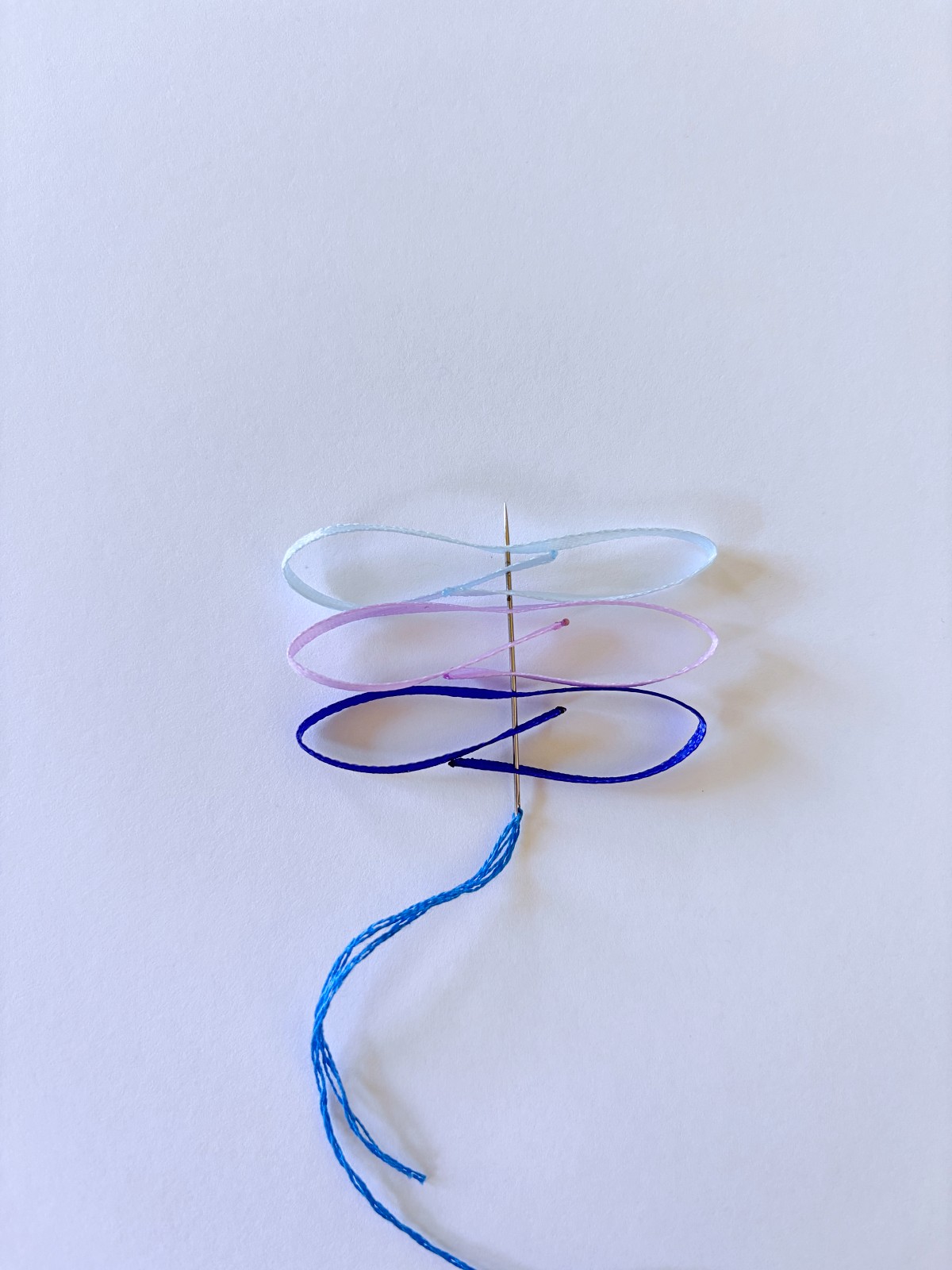 Light blue, purple, and dark blue ribbon on a sewing needle.