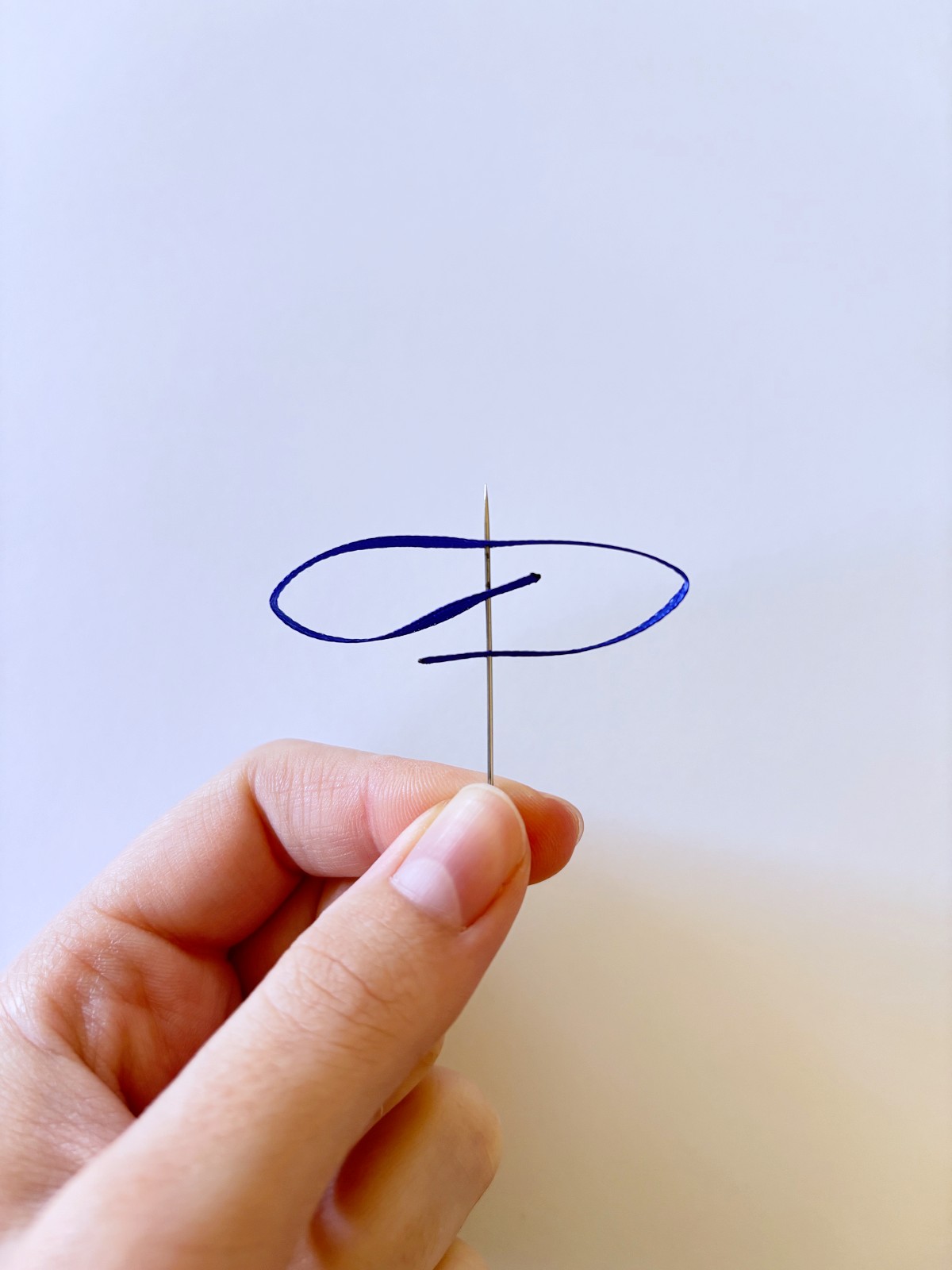 Dark blue ribbon threaded on a sewing needle.