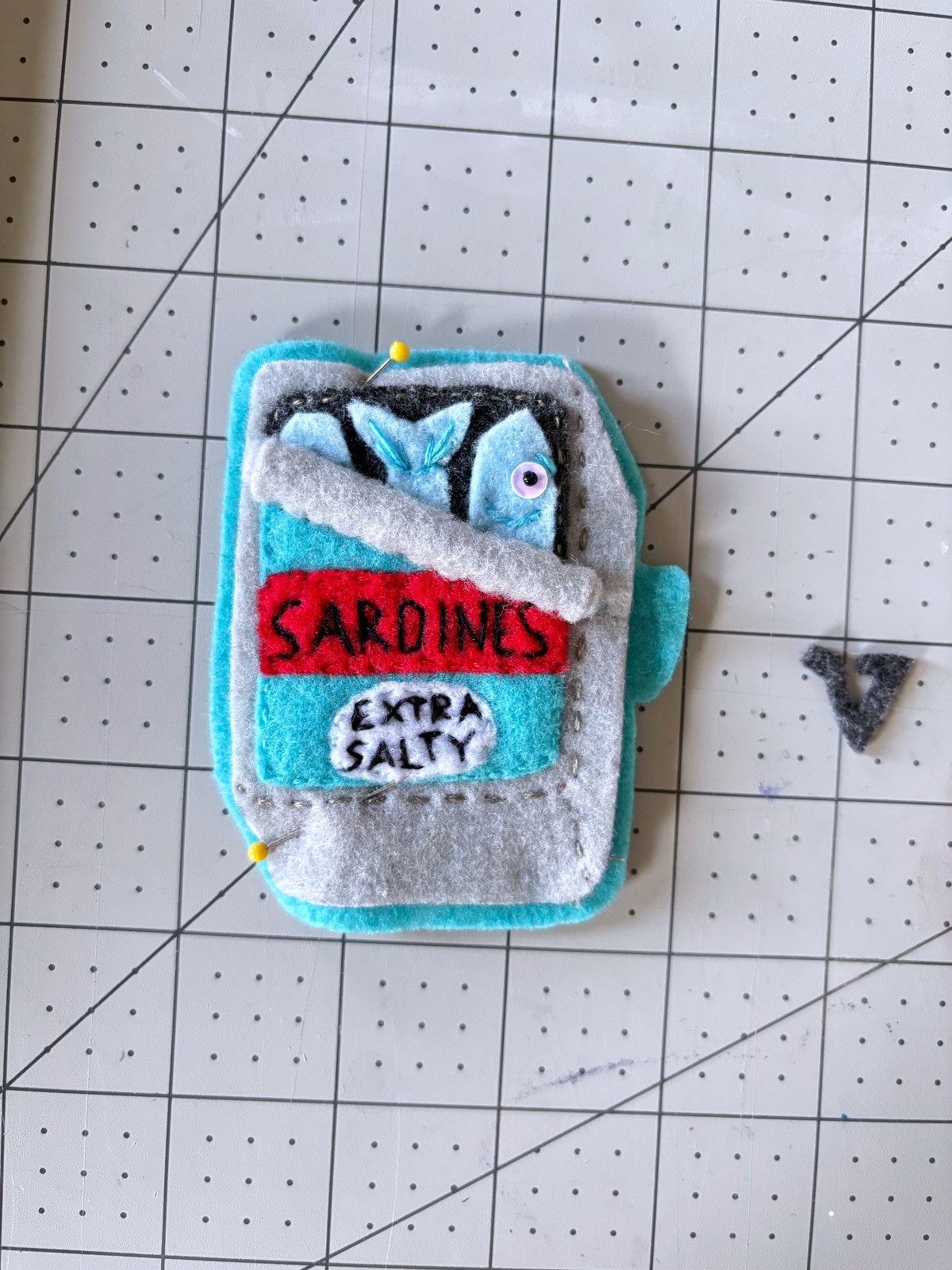 Sardine can ornament top pinned to teal felt base layer.