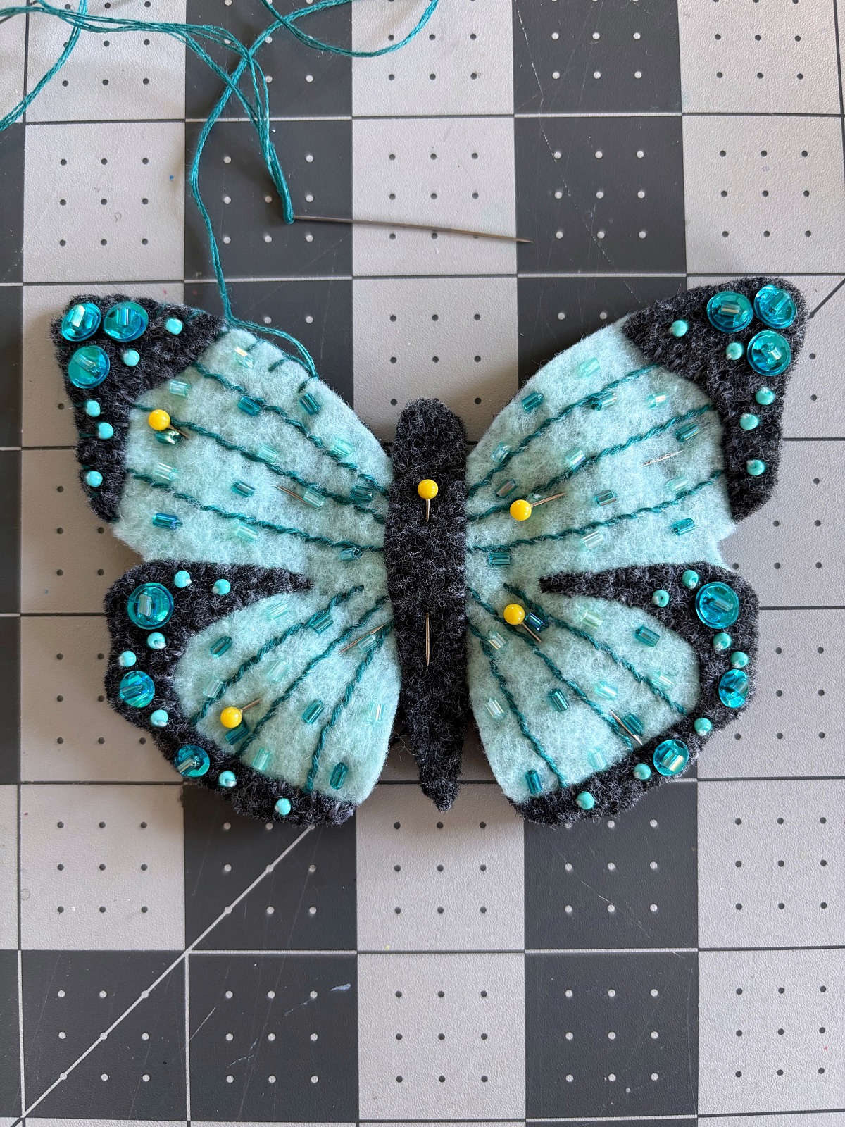 Sewing pins securing the teal butterfly to the dark gray base piece.