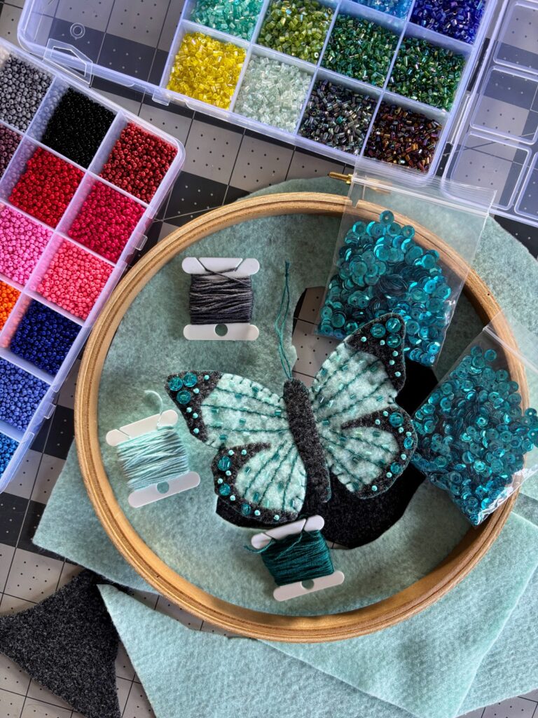 Teal butterfly ornament surrounded by beads, thread, and sequins.