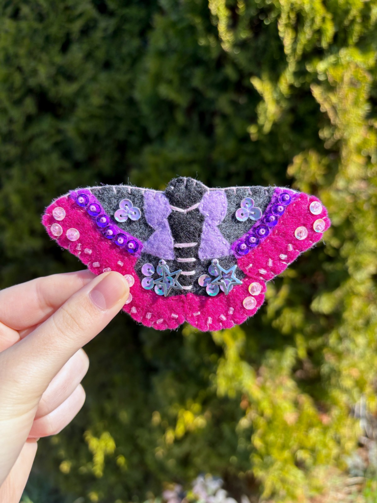 Felt moth ornament held in a hand outside.