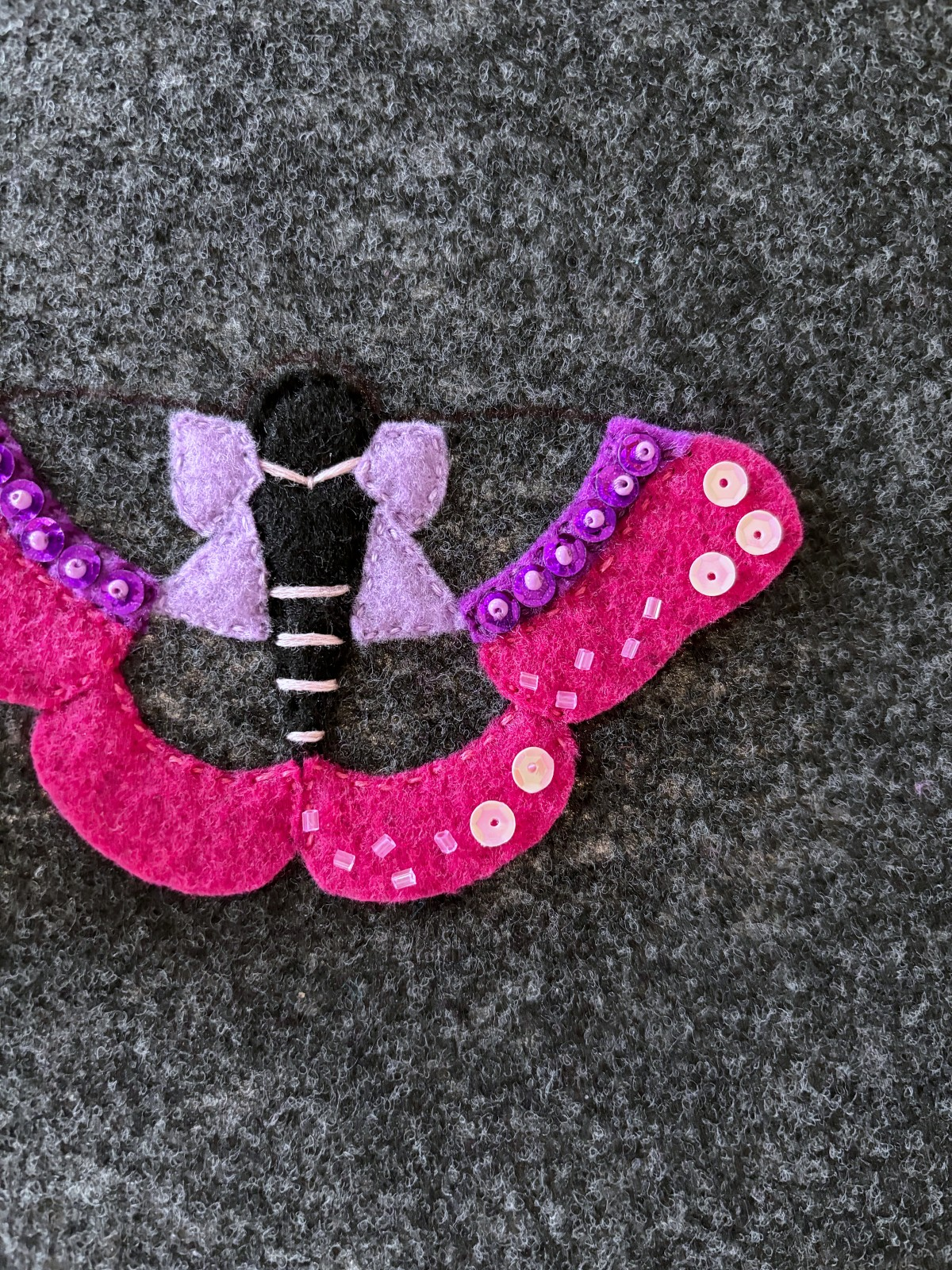 Pink sequins and tube beads placed in a pattern on the dark pink moth wing felt pieces.
