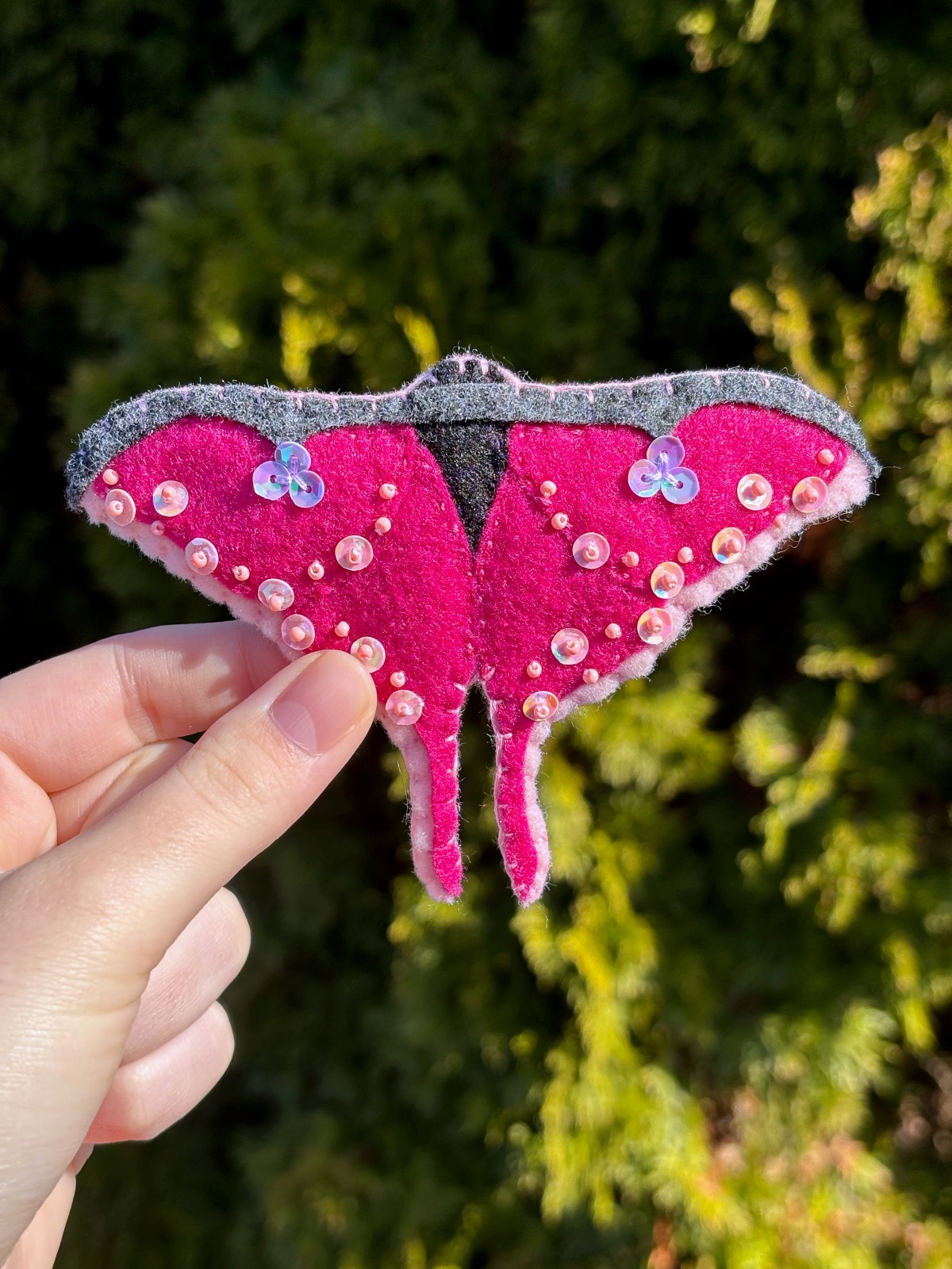 Finished luna moth ornament held by a hand, outside.