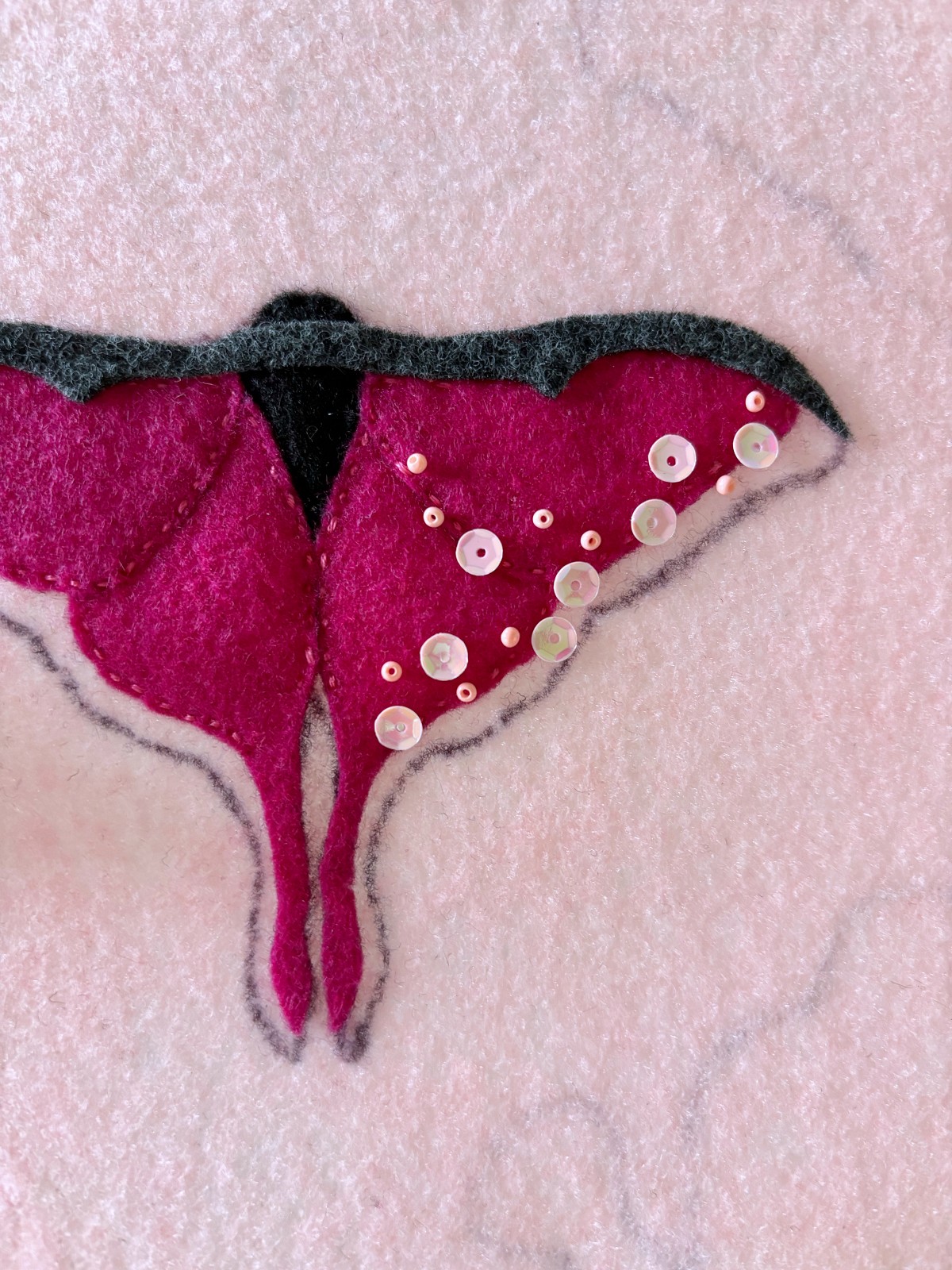 Seed beads and sequins laid out in a pattern on top of the moth wings.